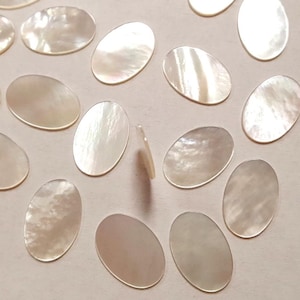 Może przedstawiać: Kolekcja owalnych, opalizujących białych kawałków muszli perłowej. Muszle są gładkie i mają naturalną, organiczną fakturę.