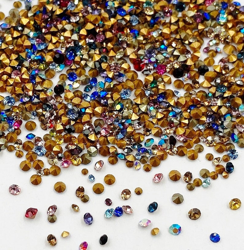 May include: A large assortment of colorful rhinestones in various shapes and sizes. The rhinestones are mostly gold, with some blue, red, and green accents.