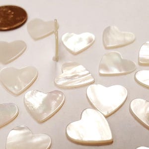 May include: A collection of white mother of pearl heart-shaped embellishments. The hearts are smooth and shiny, with a slight iridescent sheen.