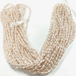 May include: A strand of off-white, oval-shaped freshwater pearls. The pearls are strung on a white thread and are approximately 6mm in size. The strand is labeled "JAPAN".