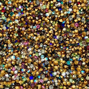 May include: A close-up of a large quantity of gold-toned metal rhinestones with clear, iridescent, and colored glass stones.