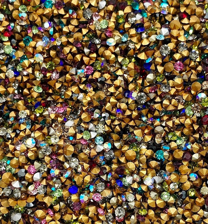 May include: A close-up of a large quantity of gold-toned metal rhinestones with clear, iridescent, and colored glass stones.
