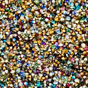 May include: A close-up image of a variety of colorful rhinestones. The rhinestones are small and have a variety of shapes and sizes. They are arranged in a random pattern and are all very sparkly.