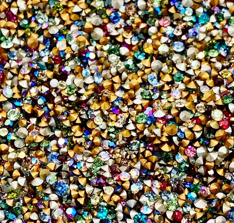 May include: A close-up image of a variety of colorful rhinestones. The rhinestones are small and have a variety of shapes and sizes. They are arranged in a random pattern and are all very sparkly.