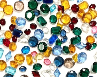 Puede incluir: Una colección de piedras preciosas facetadas sueltas de diversas formas y tamaños, incluyendo cortes redondos, ovalados, rectangulares y de diamante. Las piedras presentan una paleta de colores vibrantes en verde, amarillo, azul, rojo y transparente.