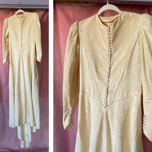May include: A vintage ivory wedding dress with a long-sleeved, fitted bodice and a flowing skirt. The dress features a button-up closure down the front and a small train.