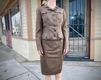 May include: A brown skirt suit with a fitted jacket and a knee-length skirt. The jacket has a button-up front and flap pockets. The skirt has a straight silhouette.