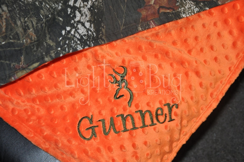May include: Orange and camouflage baby blanket with a buck head and the name "Gunner" embroidered in brown thread.