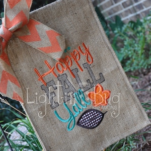 May include: A burlap fall door hanger with the text "Happy Fall Y'all" in gray and teal embroidery. The hanger is decorated with a large orange and brown bow and a small orange and brown leaf.