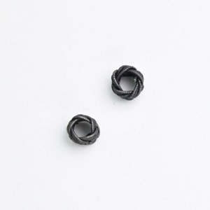 May include: Two black metal rings with a twisted design. The rings are made of a thin, flexible metal and are similar in size.