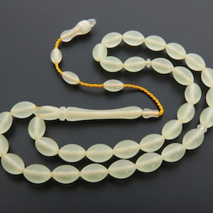 May include: A white prayer beads necklace with a tassel and a white wooden handle. The beads are oval shaped and have a translucent appearance.