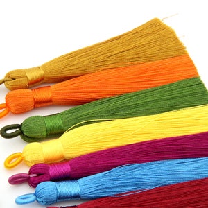 May include: Assortment of colorful silk tassels in shades of gold, orange, green, yellow, purple, blue, and red. The tassels are arranged in a row, with the gold tassel at the top and the red tassel at the bottom.