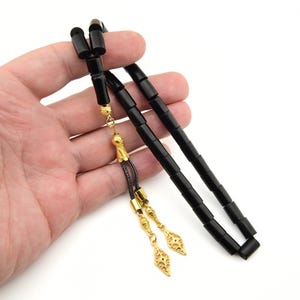 Peut inclure: Chapelet de prière noir avec des accents dorés et un gland. Les perles sont cylindriques et ont une finition lisse et polie.
