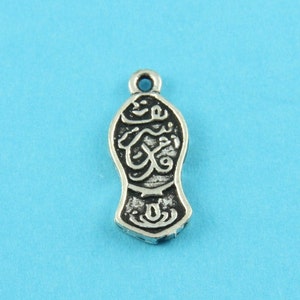 May include: A silver charm shaped like a mosque with Arabic calligraphy. The charm has a loop at the top for attaching to a necklace or bracelet.