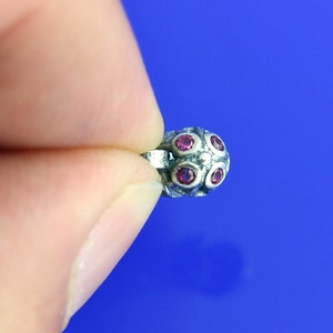 Op de afbeelding: Een zilveren neusring met vijf roze edelstenen.