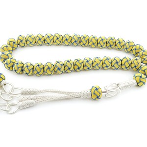 May include: A yellow and blue prayer beads, or tasbih, with a silver tassel. The beads are woven with a knot pattern.