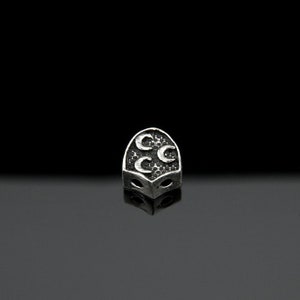 May include: A silver charm with a crescent moon design. The charm is shaped like a shield and has three crescent moons on it.