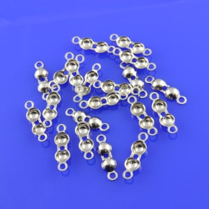 May include: A group of silver-toned metal bead caps with two loops on each side. The bead caps are scattered on a blue surface.