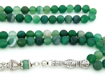 Può includere: Un rosario di preghiera in agata verde con un nappa d'argento e un ciondolo d'argento. Le perle sono rotonde e hanno un motivo a strisce.