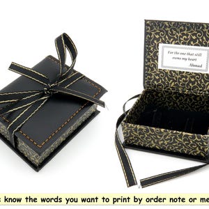 May include: A black gift box with a gold ribbon and a gold and black patterned interior. The box is open and the interior has a message that reads "For the one that still owns my heart Ahmad".
