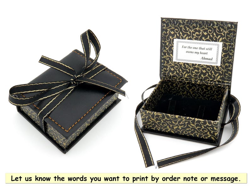 May include: A black gift box with a gold ribbon and a gold and black patterned interior. The box is open and the interior has a message that reads "For the one that still owns my heart Ahmad".