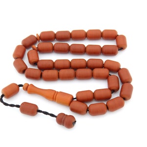 Puede incluir: Un juego de cuentas de oración con cuentas de color marrón rojizo y un mango marrón claro. Las cuentas están ensartadas en un cordón negro. El mango y la pieza final son de un tono marrón más claro. Las cuentas son de forma cilíndrica.