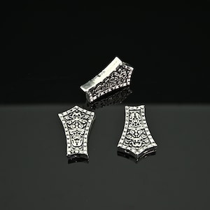 May include: Three silver-toned metal decorative pieces with intricate floral designs. The pieces are shaped like a pointed rectangle and have a textured surface.