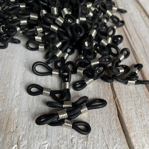 Può includere: Un mucchio di terminali per cordino per occhiali in gomma nera e argento. I terminali del cordino sono progettati per essere fissati alle montature degli occhiali.