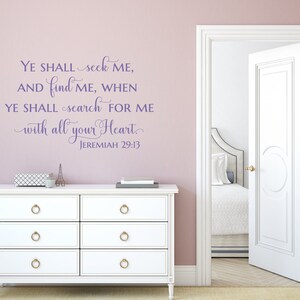 Puede incluir: Texto morado en una pared rosa claro que dice "YE SHALL seek ME, AND find ME, WHEN YE SHALL search FOR ME with all your Heart. JEREMIAH 29:13". Una c&oacute;moda blanca con pomos dorados est&aacute; en primer plano. Una puerta blanca est&aacute; abierta a una habitaci&oacute;n con una cama blanca y ropa de cama blanca.