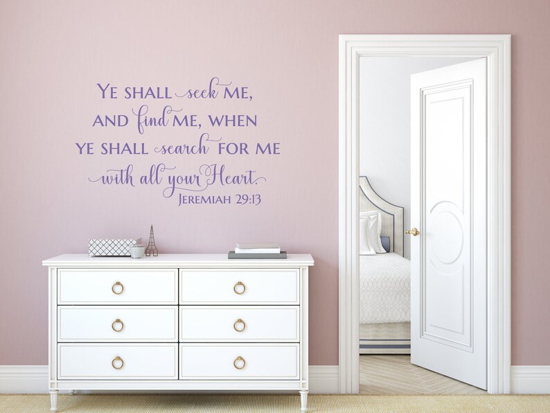Puede incluir: Texto morado en una pared rosa claro que dice "YE SHALL seek ME, AND find ME, WHEN YE SHALL search FOR ME with all your Heart. JEREMIAH 29:13". Una c&oacute;moda blanca con pomos dorados est&aacute; en primer plano. Una puerta blanca est&aacute; abierta a una habitaci&oacute;n con una cama blanca y ropa de cama blanca.