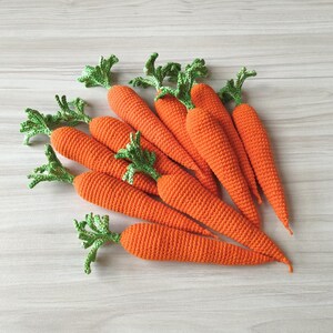 May include: A group of handmade crochet carrots in different sizes. The carrots are bright orange with green leafy tops. The arrangement is on a light-coloured wooden surface, highlighting the texture and detail of the crochet work.