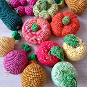 May include: A collection of crocheted fruits and vegetables, including a green zucchini, a red apple, a yellow pear, a green and white striped apple, a yellow pear, a red and orange pumpkin, a green and white striped pumpkin, a pink onion, a yellow and orange pumpkin, and a red and pink apple.