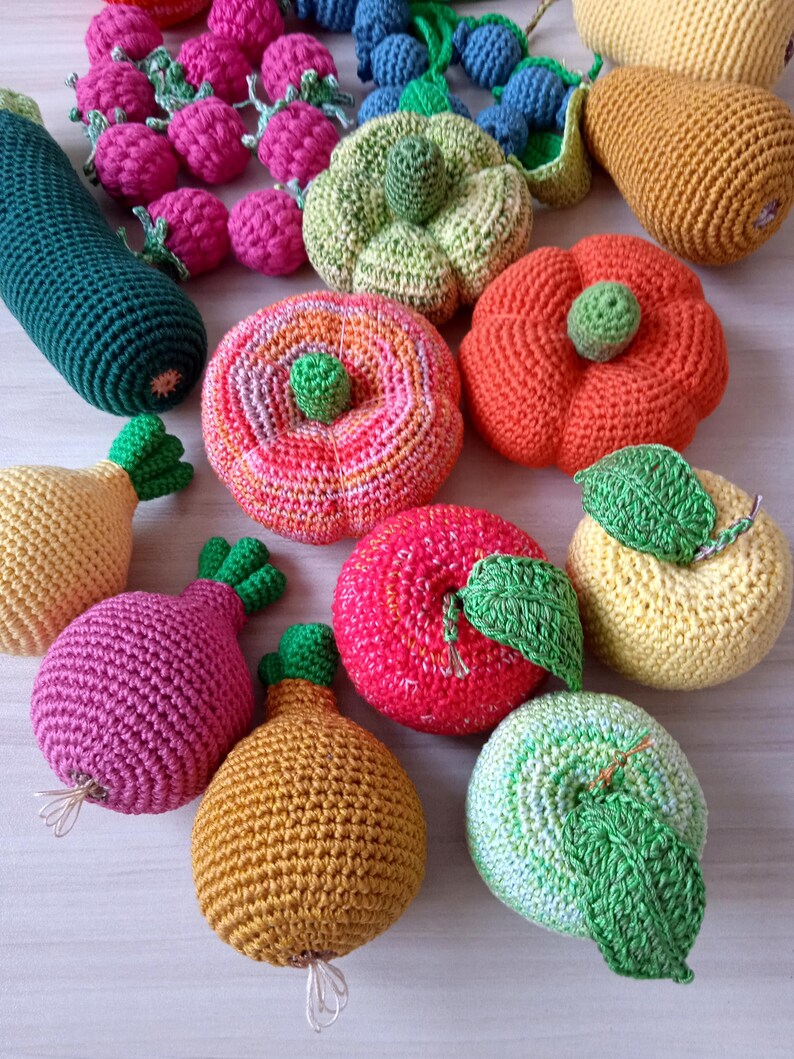 May include: A collection of crocheted fruits and vegetables, including a green zucchini, a red apple, a yellow pear, a green and white striped apple, a yellow pear, a red and orange pumpkin, a green and white striped pumpkin, a pink onion, a yellow and orange pumpkin, and a red and pink apple.