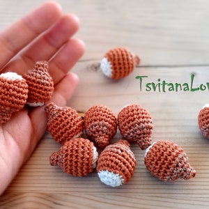 Könnte beinhalten: Acht gehäkelte braune und weiße Ornamente mit einer strukturierten Oberfläche. Die Ornamente sind in Form von kleinen Glühbirnen.