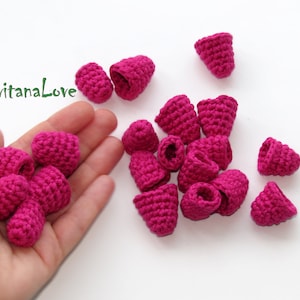 Può includere: Una mano tiene un mucchio di piccoli boccioli di fiori rosa all'uncinetto. Ci sono altri boccioli di fiori sparsi su una superficie bianca.
