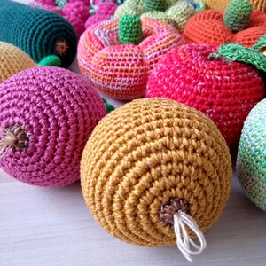 May include: A collection of crocheted fruits and vegetables, including a green zucchini, a pink beet, a yellow onion, a red apple, a green and orange pumpkin, and an orange tomato.
