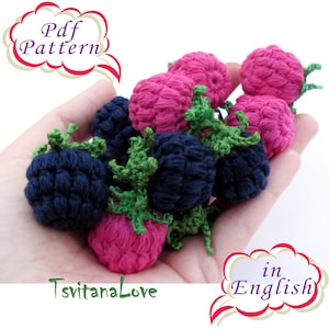 Peut inclure: Gros plan d'une main tenant un groupe de framboises et de mûres crochetées. Les framboises sont roses et les mûres sont bleu foncé. Les fruits crochetés sont disposés en grappe, certaines baies se chevauchant. L'image comprend le texte "Pdf Pattern" et "TsvitanaLove".