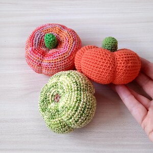 May include: Three crocheted pumpkins in different colors and patterns. The pumpkins are orange, green, and pink with orange and green stripes.