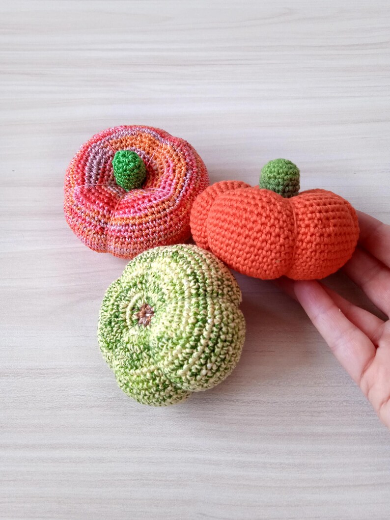 May include: Three crocheted pumpkins in different colors and patterns. The pumpkins are orange, green, and pink with orange and green stripes.