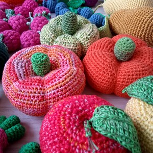 May include: A collection of crocheted fruit and vegetables, including apples, pears, pumpkins, and grapes. The fruits and vegetables are all different colors and have a variety of textures.