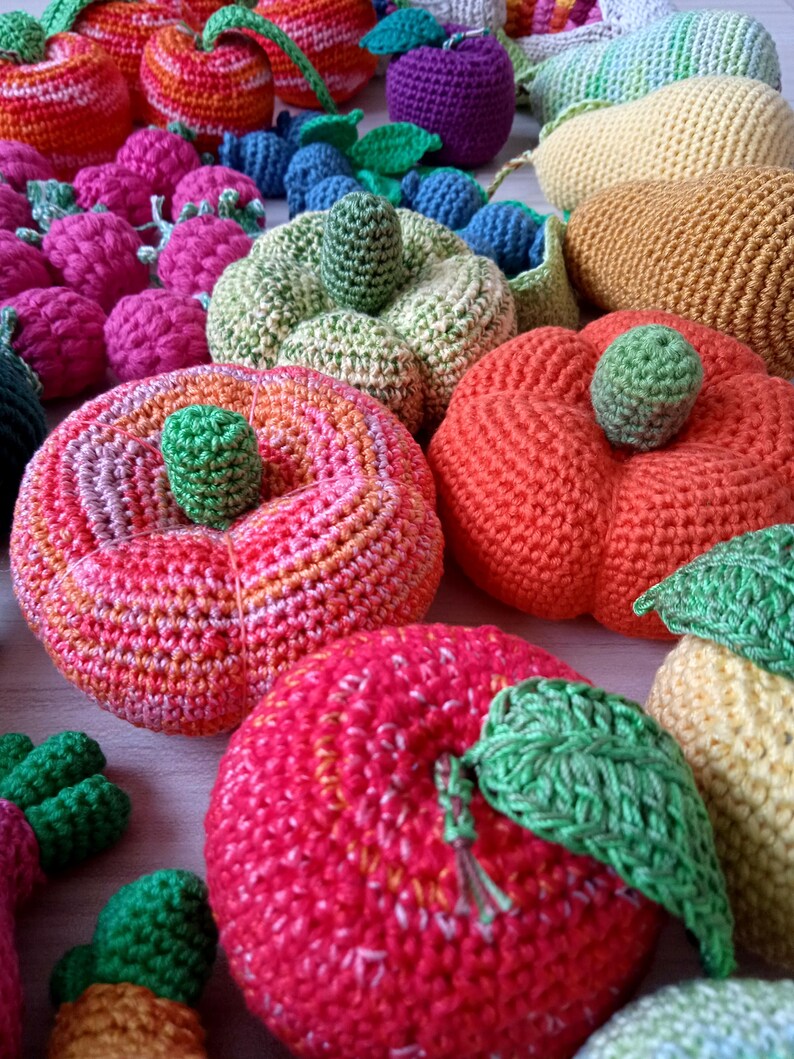 May include: A collection of crocheted fruit and vegetables, including apples, pears, pumpkins, and grapes. The fruits and vegetables are all different colors and have a variety of textures.