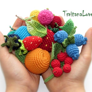 May include: A collection of crocheted fruits and berries, including strawberries, blueberries, raspberries, and an orange, in a variety of colors. The crocheted fruits are arranged in a person's hands.