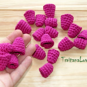 May include: A collection of 17 crocheted raspberry-shaped ornaments in a vibrant pink color. The ornaments are arranged on a wooden surface and in a hand.