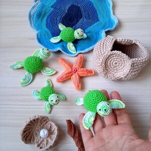 Op de afbeelding: Een verzameling handgemaakte haakartikelen met een oceaanthema. Bevat groene schildpadden, een zeester, een zeeschelp en een blauw-witte oceaanvormige mat. De items zijn gemaakt met kleurrijk garen en zijn gerangschikt op een lichtgekleurd oppervlak.