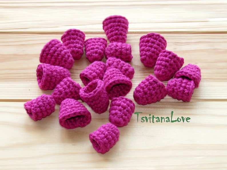 May include: A collection of 17 crocheted pink flower-shaped embellishments. The embellishments are made of yarn and have a textured surface.