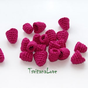 May include: A collection of 15 crocheted raspberry shapes in a vibrant pink color. The raspberries are arranged in a cluster on a white surface.