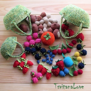 May include: A collection of crocheted fruits and vegetables, including strawberries, blueberries, raspberries, cherries, a persimmon, and mushrooms, displayed in two green crocheted baskets. The items are arranged on a wooden surface.