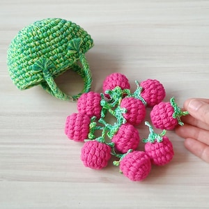 Pode incluir: Uma cesta de crochê verde com alça e um cacho de framboesas de crochê rosa.