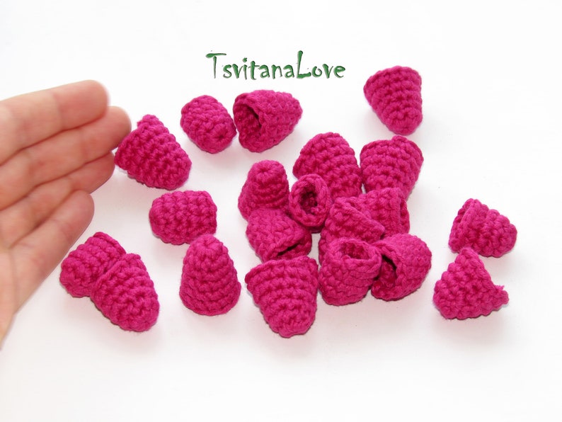 May include: A collection of 18 crocheted raspberry-shaped embellishments in a vibrant pink color. The embellishments are made with a fine yarn and have a delicate texture.