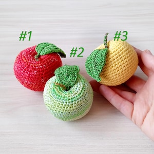 Könnte beinhalten: Drei gehäkelte Obstspielzeuge, ein roter Apfel, ein grüner Apfel und eine gelbe Zitrone. Jedes Obst hat ein grünes gehäkeltes Blatt.